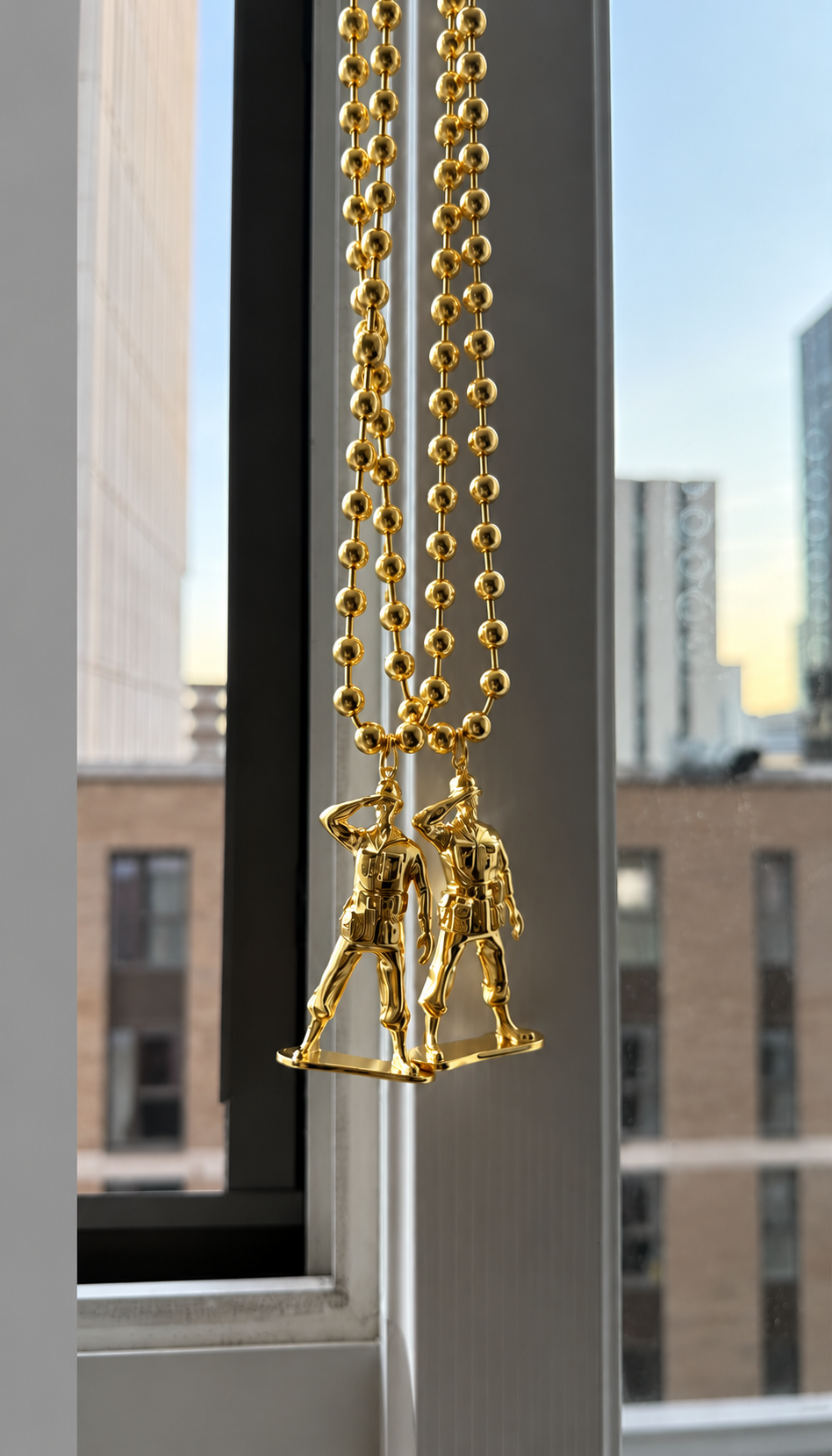 Two gold plated soldier chains hanging in a window above a city skyline